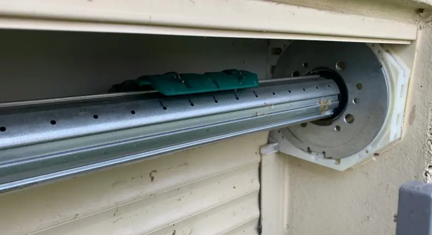 Détail du mécanisme d'un volet roulant, prêt pour comment démonter un moteur de volet roulant. Le tube métallique est visible, avec un support vert.