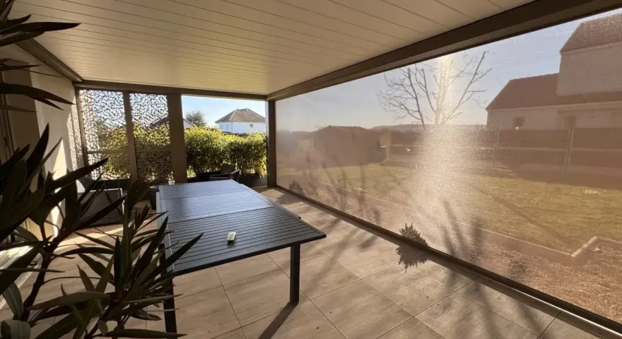 Terrasse avec table et chaises, sous un abri moderne. La menuiserie RAL 7006 s'intègre parfaitement au paysage.