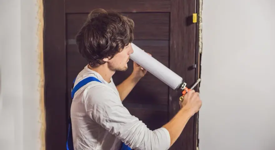 Un homme utilise une mousse expansive pour isoler une porte en bois.