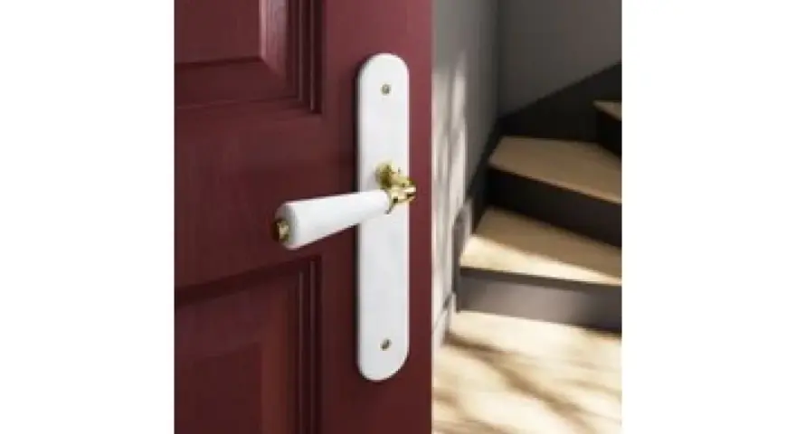 Poignée de porte blanche sur fond bordeaux, avec un escalier en bois visible. Quelle couleur de poignée pour porte blanche ? L'or brille.