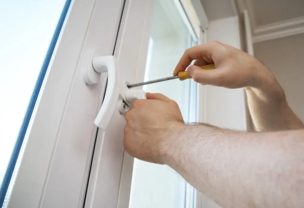 Main tenant utilise un tournevis pour changer la poign&eacute;e d'une fen&ecirc;tre en aluminium.
