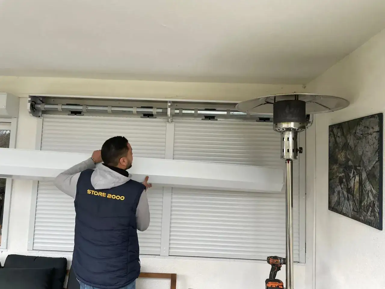 Un technicien de Store 2000 s'appr&ecirc;te &agrave; changer un volet roulant &eacute;lectrique, travaillant sur le m&eacute;canisme sup&eacute;rieur.