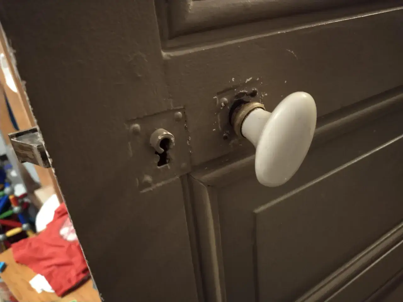 Gros plan sur le m&eacute;canisme poign&eacute;e porte ancienne, avec une poign&eacute;e blanche et une serrure visible.