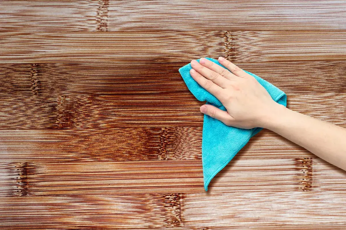 Main d'une personne utilisant un chiffon bleu pour nettoyer une surface en bois. Apprenez comment nettoyer des portes en bois pour un éclat parfait.
