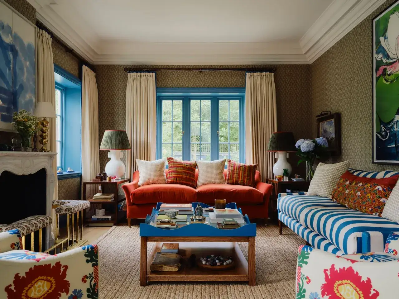 Salon confortable avec canap&eacute; orange, fauteuils fleuris et table basse bleue. La couleur encadrement fen&ecirc;tre int&eacute;rieur est d'un bleu vif, contrastant avec les rideaux cr&egrave;me.