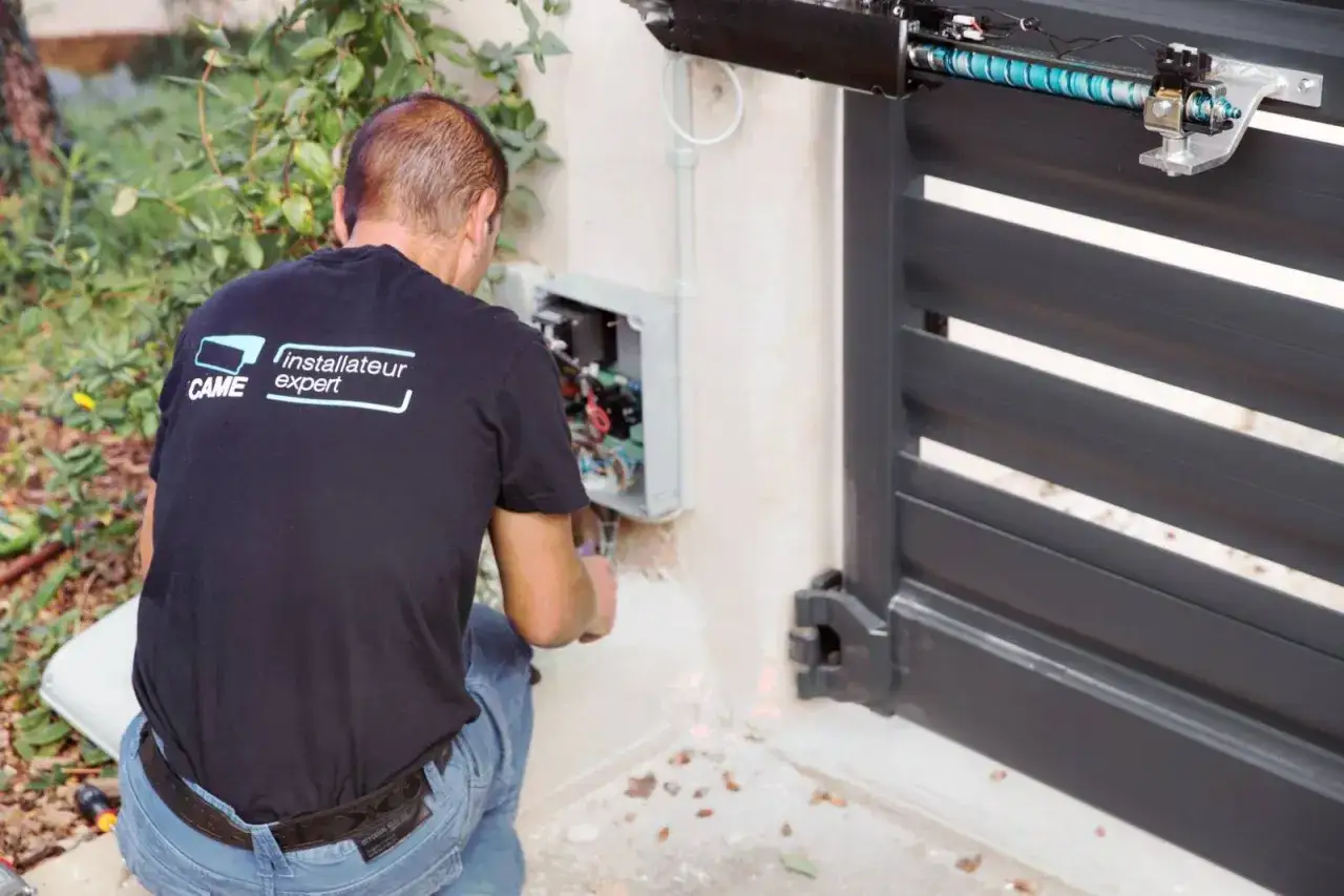 Un technicien CAME répare un portail dea bloqué. Il travaille sur le boîtier de commande ouvert.