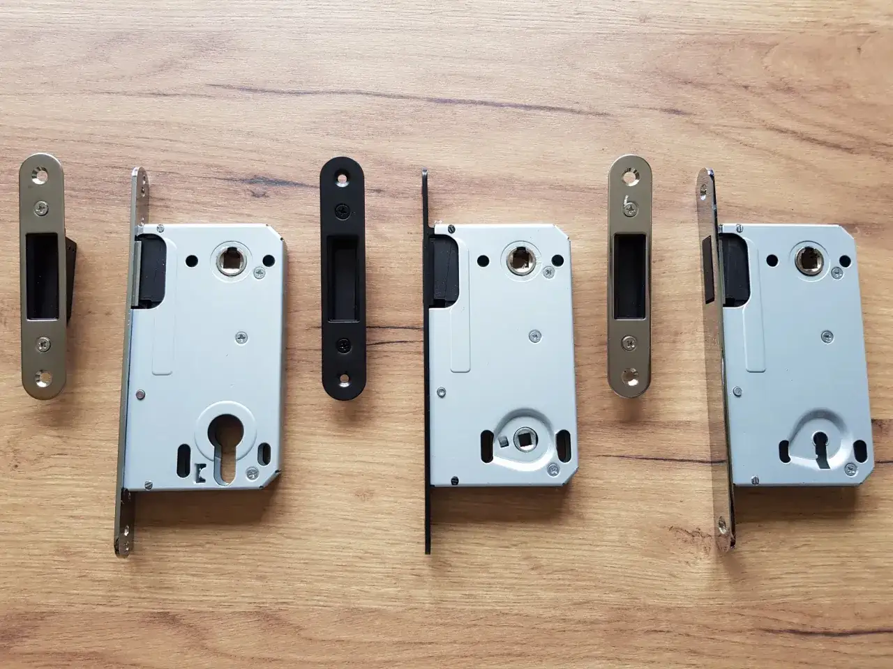 Ensemble de serrures pour porte int&eacute;rieure, avec leurs g&acirc;ches, sur fond de bois.