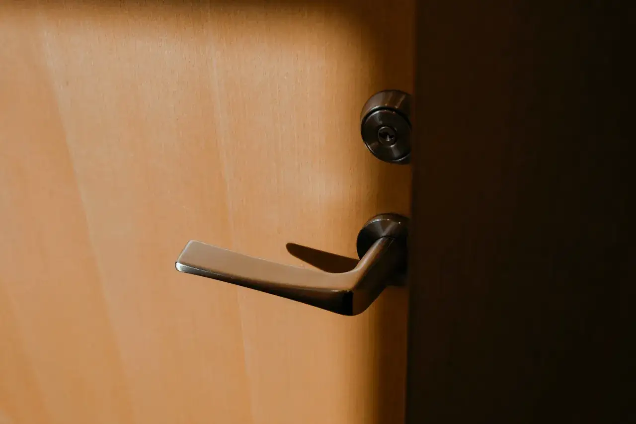 Poignée de porte en bois clair avec serrure 3 points. La poignée est en métal brossé et semble bloquée, ne remonte plus.