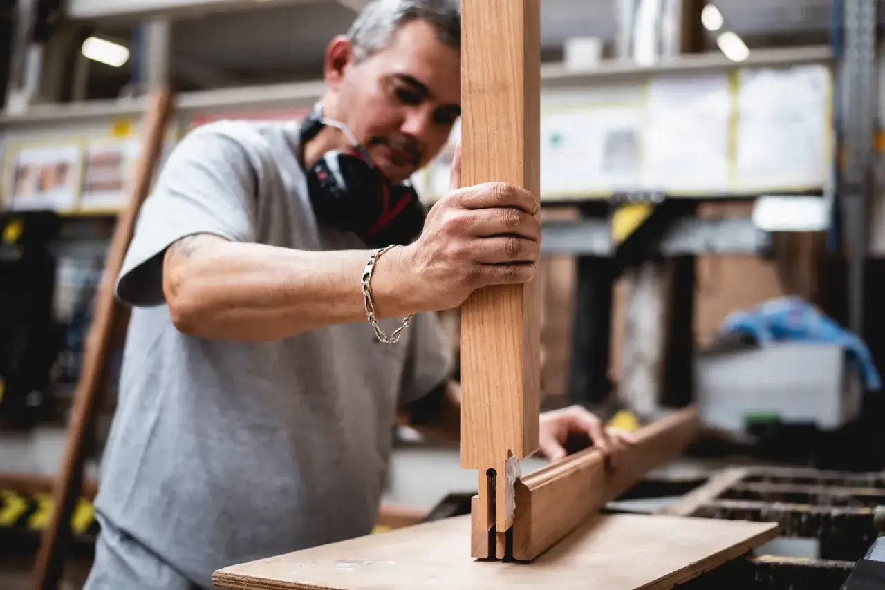 Artisan assemblant des pi&egrave;ces de bois pour fabriquer une fen&ecirc;tre. Il tient une pi&egrave;ce verticale et une pi&egrave;ce horizontale, pr&ecirc;t &agrave; les joindre.