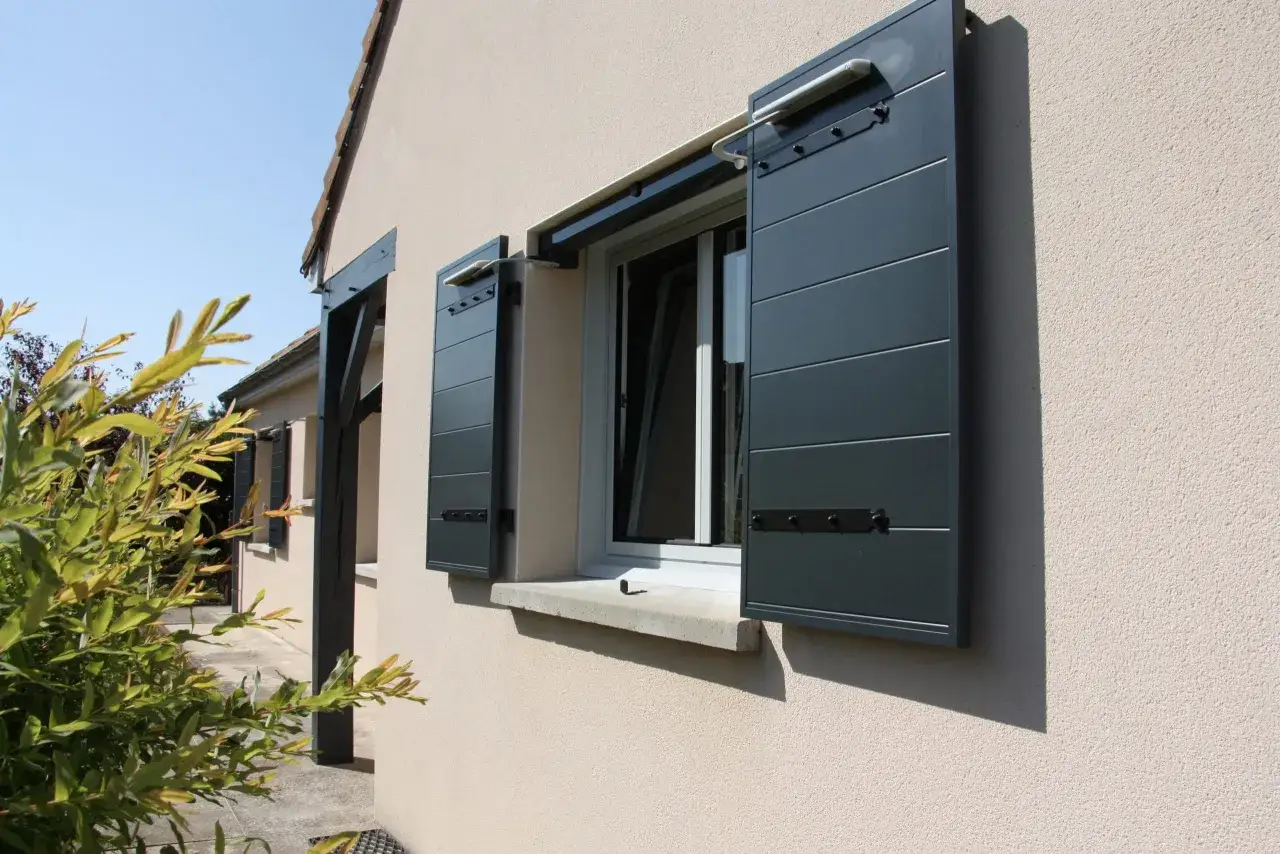 Volets gris anthracite ouverts sur une fenêtre, avec un mécanisme de type de motorisation visible.