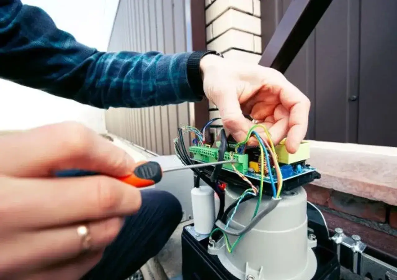 Réparation du circuit d'un portail électrique bloqué ouvert. Un tournevis ajuste les fils colorés.