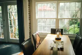 Le **couleur encadrement fenêtre intérieur** blanc met en valeur la lumière naturelle baignant la salle à manger. Des chaises en cuir marron entourent une table en bois.