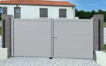 Portail battant gris clair RAL 7035, moderne et discret, s'ouvrant sur une cour pavée devant une maison blanche aux volets gris.