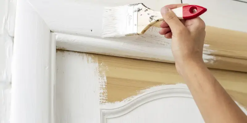 Une main applique de la peinture blanche sur une porte en bois, transformant son aspect.